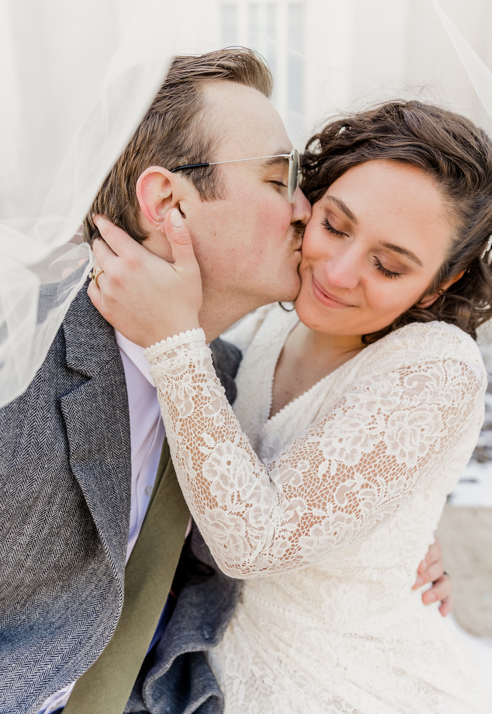 Groom plants a kiss on bride's cheek as she smiles and cups his face with her hands, captured by Robin Kunzler Photo