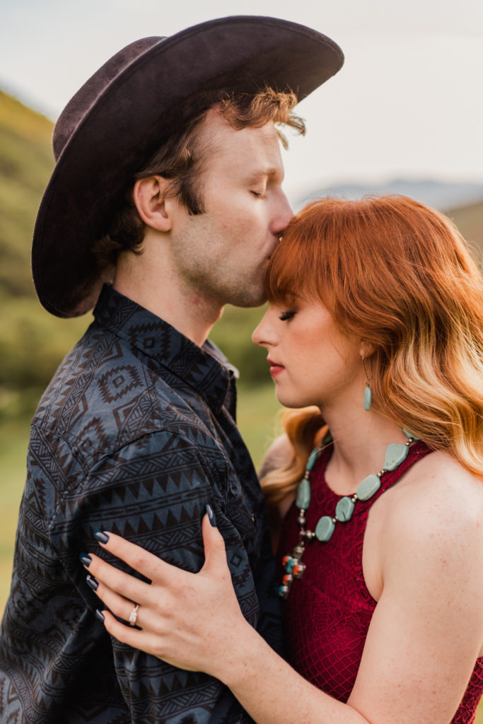 Jayson gives Jessica a forehead kiss in the green hills of Logan, Utah for their engagement photos taken by Robin Kunzler Photo.