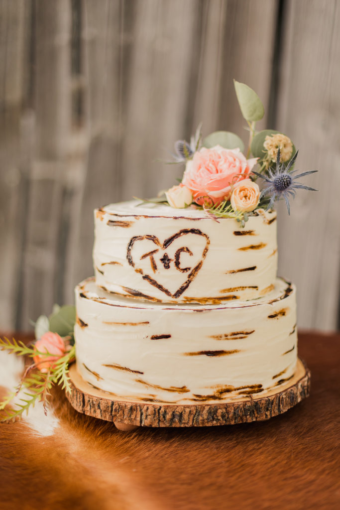 Two-tier wedding cake with flower decorations and engraving of T+ C inside heart
