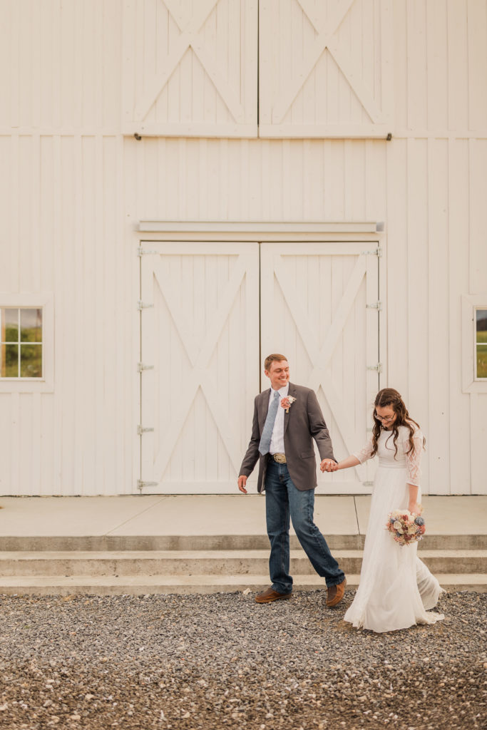 Couple holding hands in front of barn in Utah during their wedding shoot