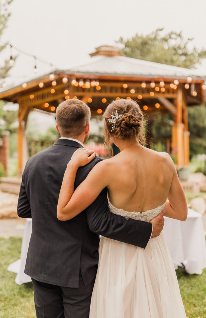 Bride and groom standing close to each other with their backs to the camera and facing the gazebo