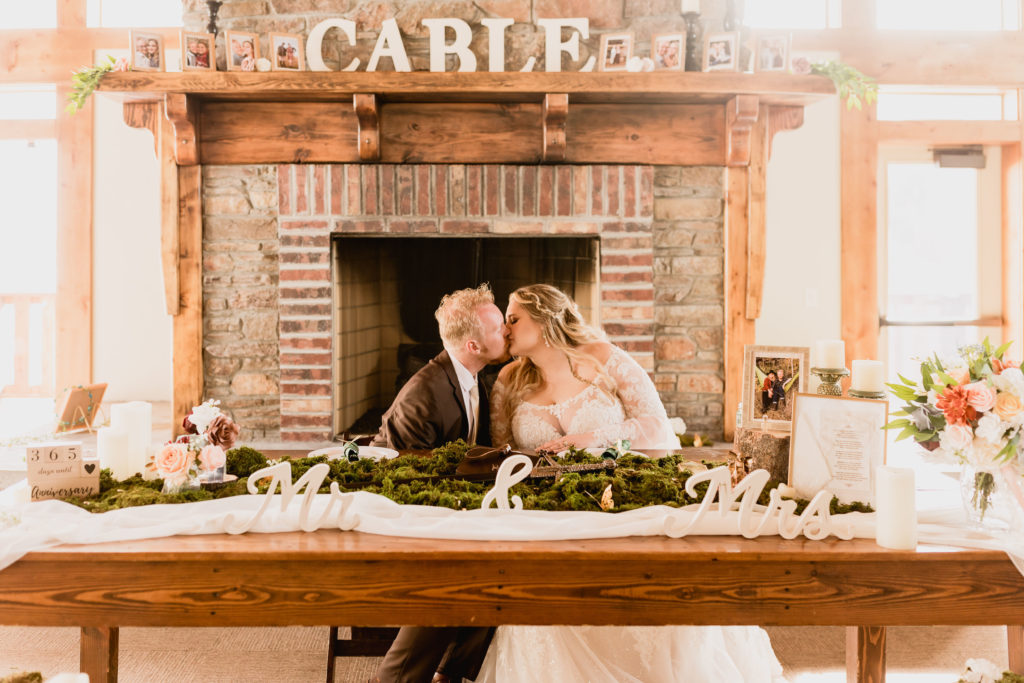 Bride and groom sharing a kiss at their wedding reception table, captured by Robin Kunzler Photo